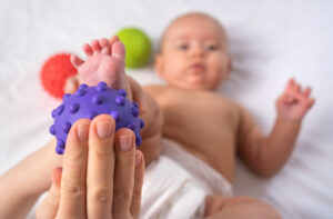 imagem ilustrativa de bebe recebendo uma massagem nos pés com uma bolinha de estimulo sensorial